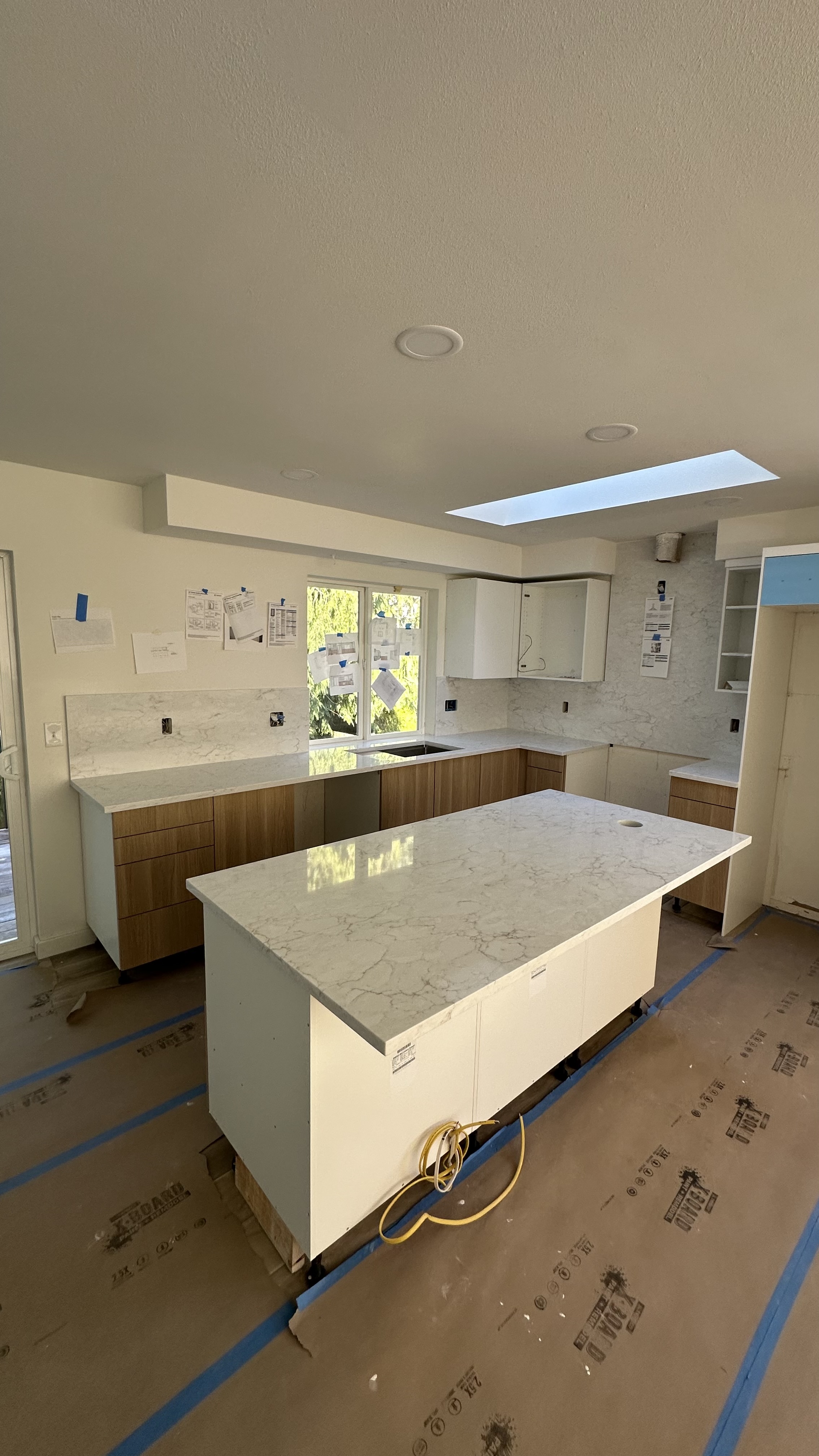 Natural wood kitchen cabinetry with a large pale stone island, countertops, and full-height backsplash installed by Viko Enterprise