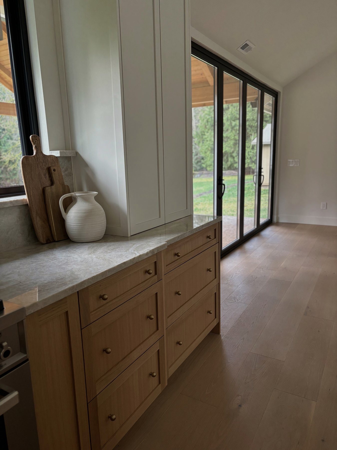 Taj Mahal quartzite counter installed over custom natural wood cabinetry beside large black-framed doors