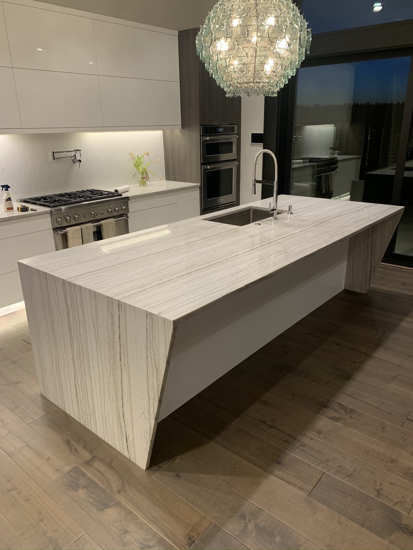 Finished white stone kitchen island with waterfall ends and a full-height slab backsplash